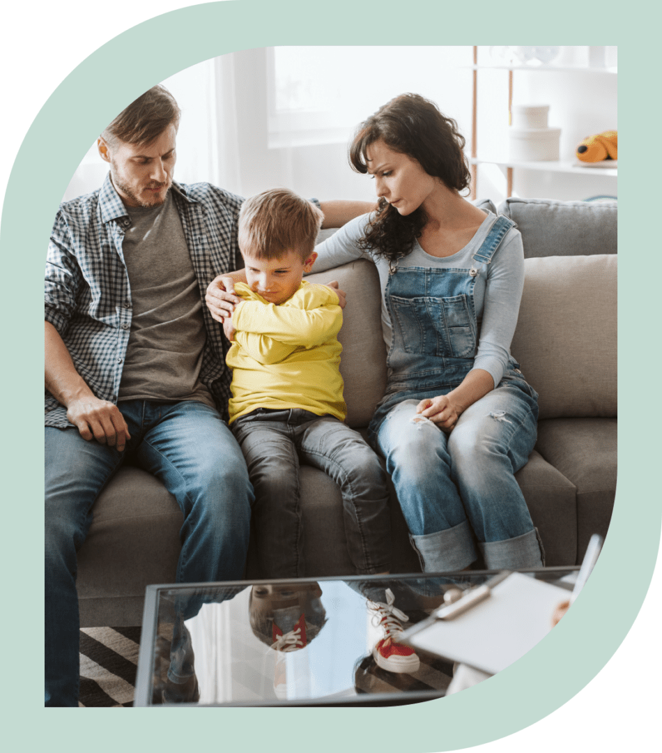 Family comforting sad child on sofa.