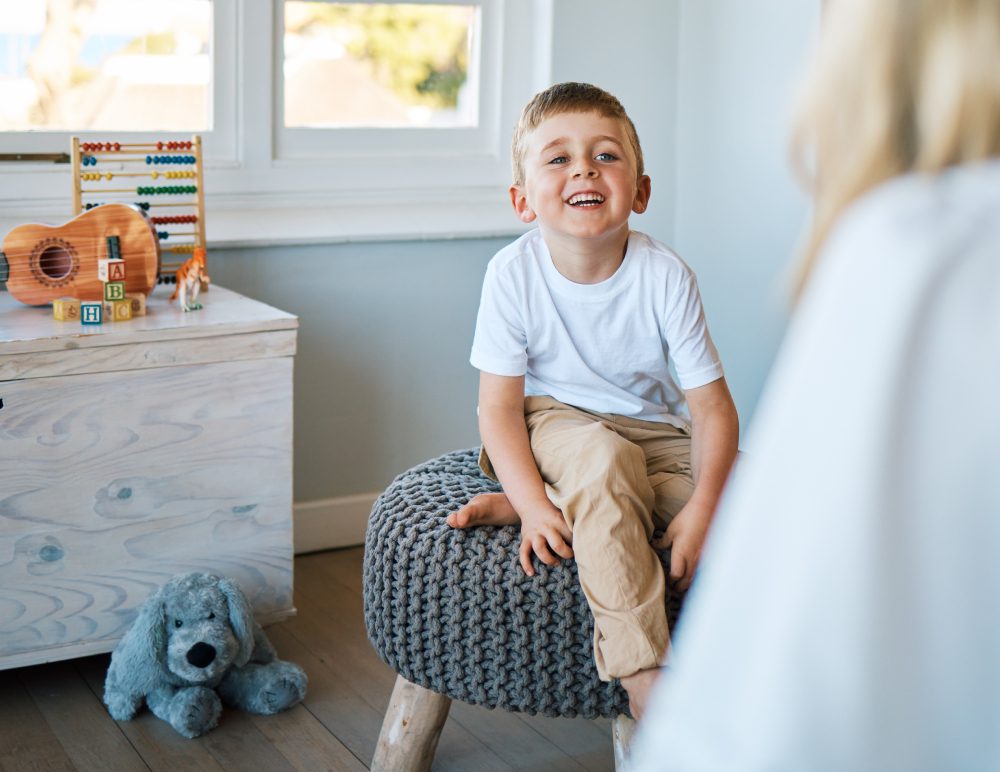 Child smiling while sitting on a stool.